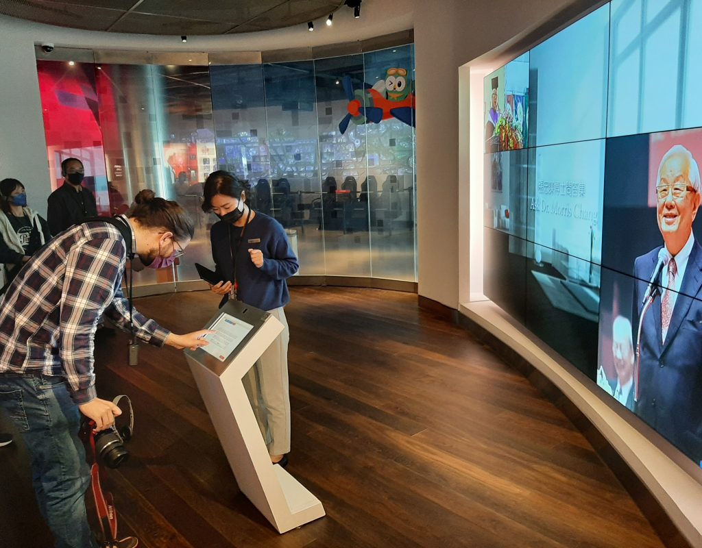 Student Lukas beugt sich im TSMC-Museum über einen Bildschirm. Eine Videowand zeigt Unternehmensgründer Morris Chang.