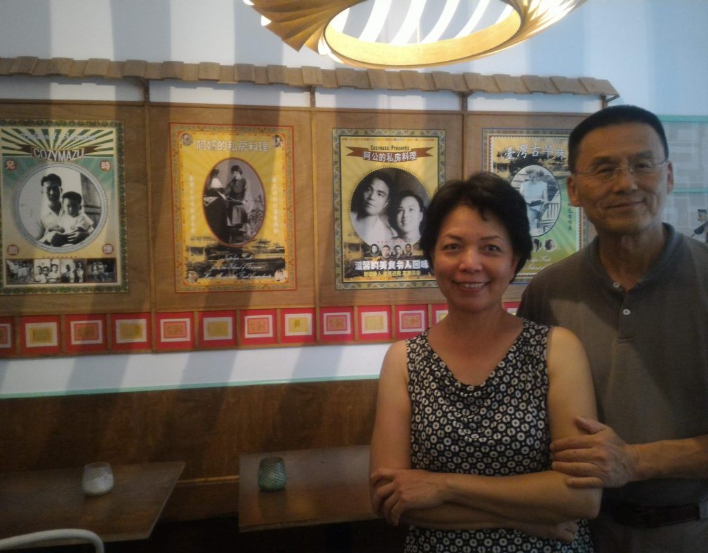 Das Ehepaar Chan steht vor einer Wand, die mit alten Schwarzweiß-Fotos aus Taiwan dekoriert ist.